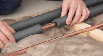 copper pipe being covered with form insulation in loft