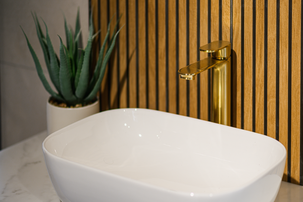 Oceanair Perth Showroom Bathroom Design. White contemporary rectangular bowl basin, gold basin mixer tap, wood panelling, marble effect sink-top, faux succulent plant in white pot.