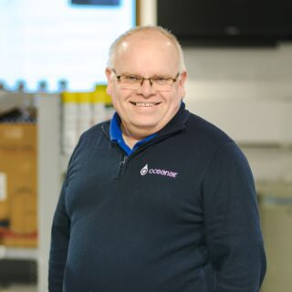 Man wearing a navy blue sweater with a logo, standing in an indoor setting.